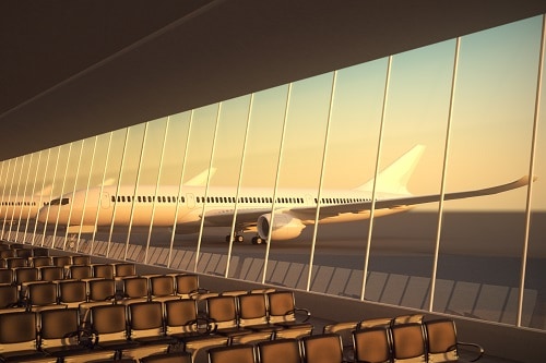 Terminal del aeropuerto moderno con asientos de cuero negro al atardecer. Una gran fachada de vidrio de visión con un avión de pasajeros detrás de él.